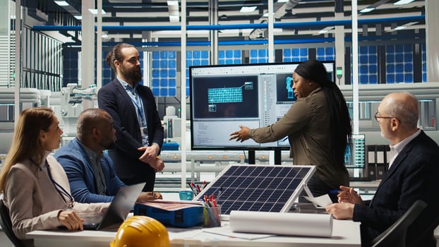 Photovoltaics researchers doing meeting, looking at monitor, evaluating solar cells to improve energy production. Experts optimizing factory equipment for better energy absorption, camera A photo