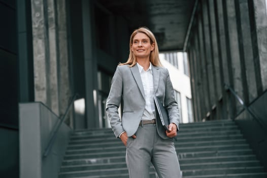Holding laptop ,in ,hands, standing. Woman in formal clothes is outdoors near the business building photo