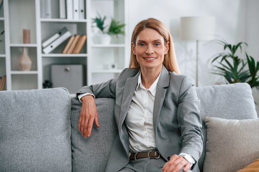 Front view. Woman in formal clothes is at home, sitting on the sofa photo