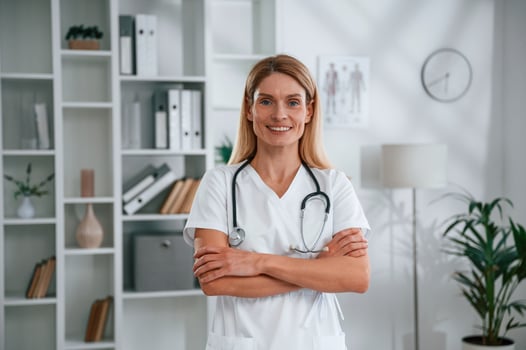 Standing with arms crossed.. Young, female doctor in white coat is indoors photo
