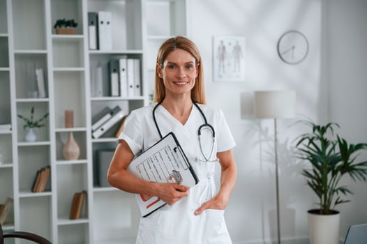 With documents in hands. Young female doctor in white coat is indoors photo