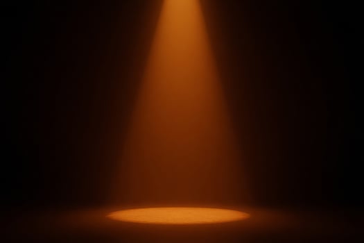 A beam of orange light shines down onto a circular spot on the ground, illuminating it brightly in a dark room photo