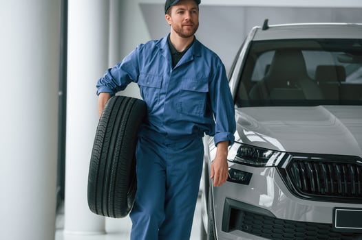 With tire in the hands. .Man in blue uniform is working in the car service photo