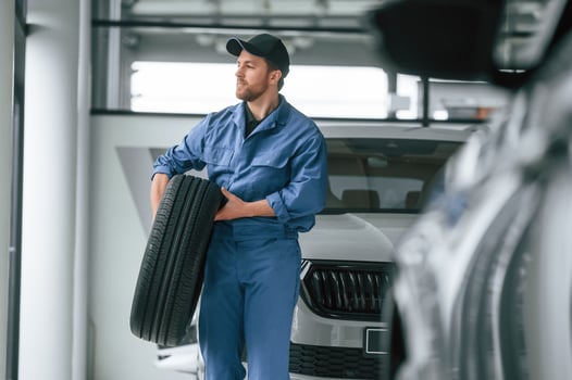 With tire ,in the hands. Man in blue ,uniform is working in the car service photo