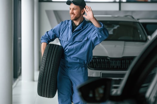 Walking forward, and holding the tire. .Man in blue uniform is working in the car service photo