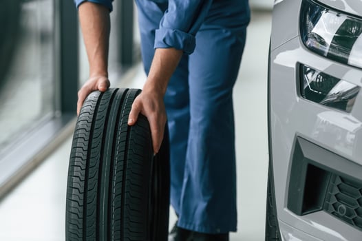 Close up, view. Moving the tire. Man in blue uniform is working in the car service photo