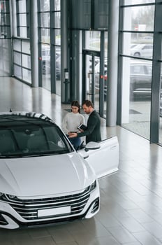 Man is showing ,the new automobile to the woman customer in the car dealership photo