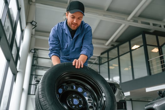 Front view, moving the, tire. Man ,in blue uniform is working in the car service photo