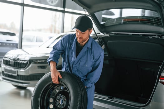 Putting the, tire out of ,automobile. Man in blue uniform is working in the car service photo