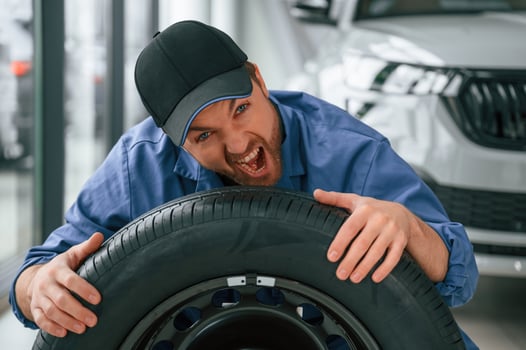 Having ,fun, smiling, with, tire. Man in blue uniform is working in the car service photo