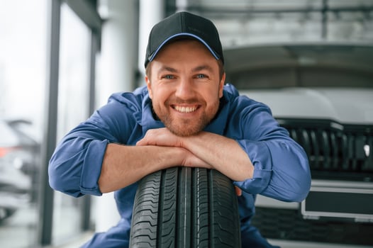 Leaning, on, the, tire and smiling. Man in blue uniform is working in the car service photo