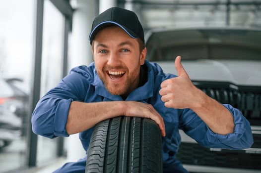 Leaning on the, tire and, smiling. Man in blue uniform is working in the car service photo