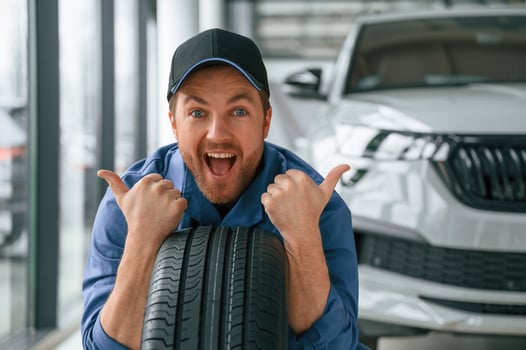 Leaning on the tire and smiling. Man in blue, uniform is working in the car service photo