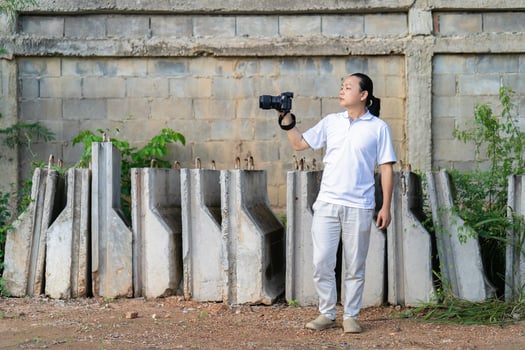 Professional Asian Chinese - Thai Camera man posture 12and focus in viewfinder and LED screen on mirrorless camera medium format in construction concrete area. photo