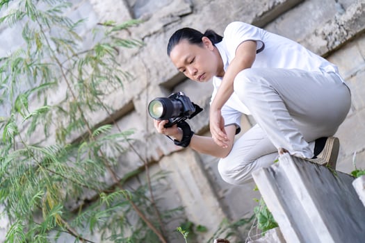 Professional Asian Chinese - Thai Camera man posture 6and focus in viewfinder and LED screen on mirrorless camera medium format in construction concrete area. photo