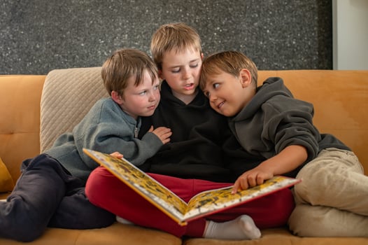 A cozy scene of three boys sitting on a couch, with the eldest reading a book and the younger ones listening intently photo