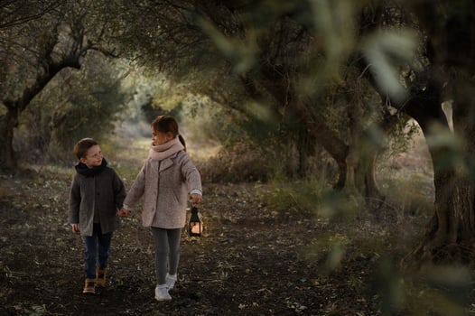 In a dreamy forest tunnel, a girl and boy wander slowly, their lantern casting soft shadows around them. photo