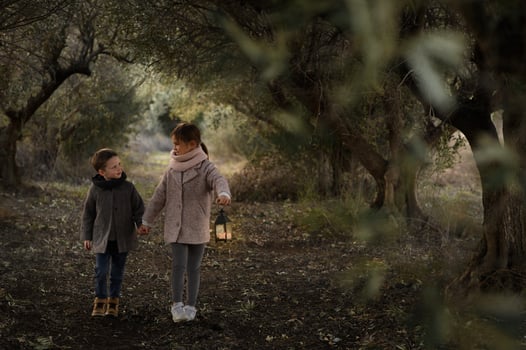 A boy and girl walk hand in hand through a magical forest tunnel, a glowing lantern lighting their path. photo