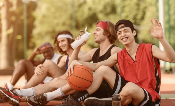 Asian player and his multinational team having rest on basketball arena outdoors, empty space. Panorama photo