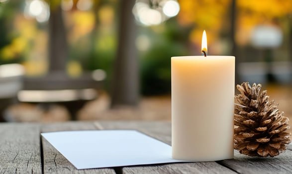A serene setting with a lit candle, pine cone, and blank paper outdoors. photo