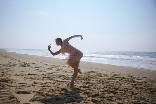 Dancer in motion on wide sandy beach under bright sky near ocean waves photo