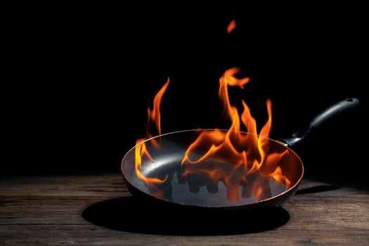 Black cooking pan with flames placed in kitchen on dark background table.. photo