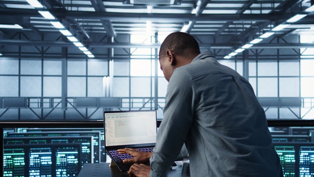 Engineer coding on laptop, optimizing resource utilization, adjusting power management settings. Server room worker maintaining stable infrastructure using notebook, camera B photo