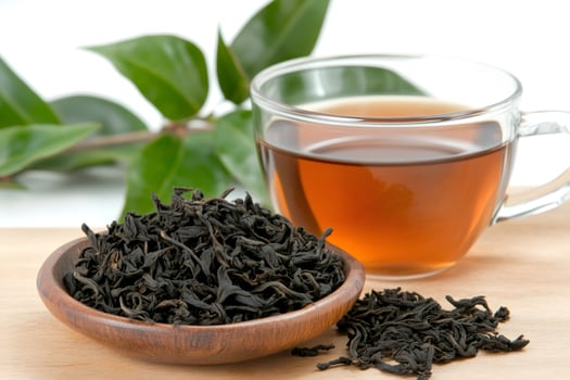 Dried tea leaves resting in small wooden bowl near cup of tea photo