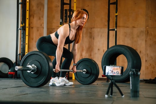 With barbell. Shooting by smartphone. Beautiful strong woman is in the gym photo
