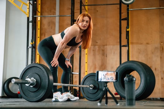 With barbell. Shooting by, smartphone. Beautiful strong woman is in the gym photo