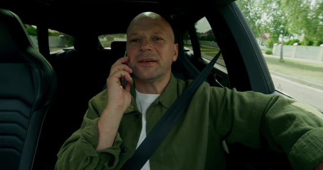 A man is talking on a mobile phone when driving a car. He's smiling. Front view in the car interior. Summer day photo