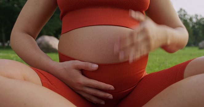 A pregnant woman in red is sitting on the grass photo