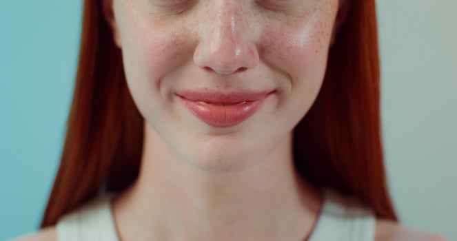 A red-haired woman with freckles is smiling at the camera while standing on a studio background. Close-up of her mouth photo