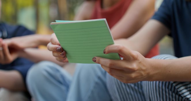 A woman holds cards with notes in her hands, sitting on the university steps next to her friends. Close-up of her hands, unrecognizable persons photo