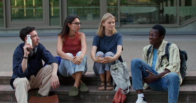 A group of young people are talking while sitting on the university steps on a summer day photo