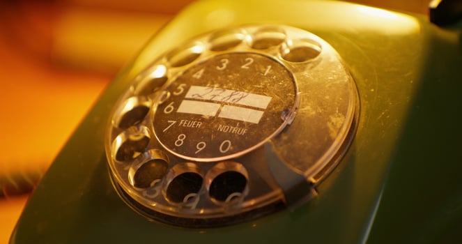 The finger dials a number on an old wired phone. Close-up photo