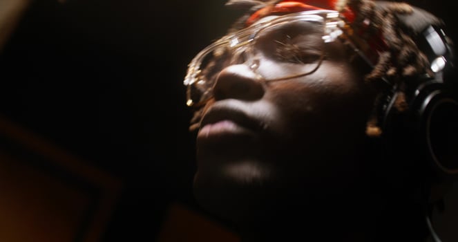 A man wearing headphones and glasses in a recording studio photo