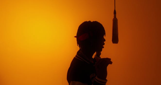 A stylish young man sings into a hanging microphone. Studio on an orange background photo