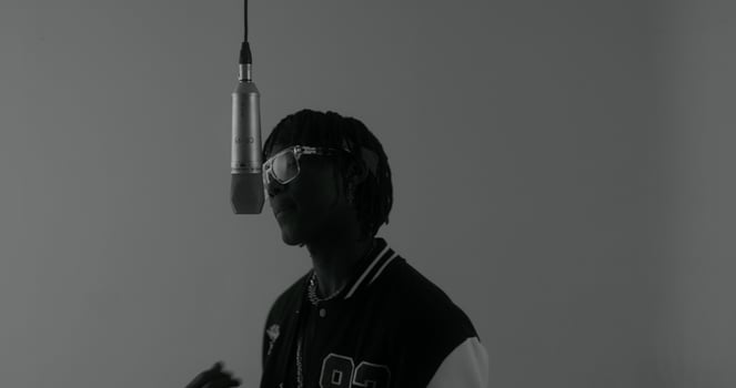 Recording a clip. The rapper sings into a hanging microphone. Black and white photo