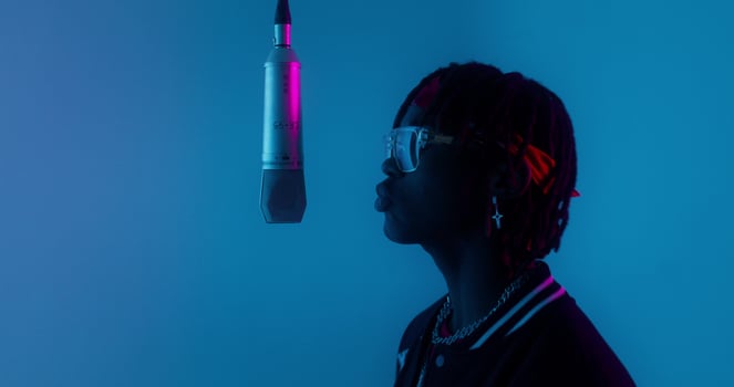 Recording a clip. The rapper sings into a hanging microphone standing on a blue background in the studio photo
