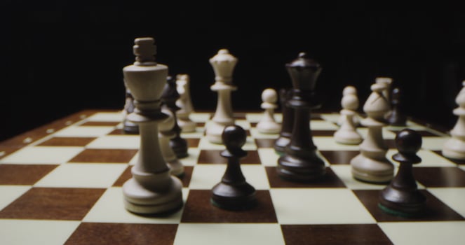 Black and white chess pieces stand on the chessboard in a chaotic manner, in the process of the game, close up photo