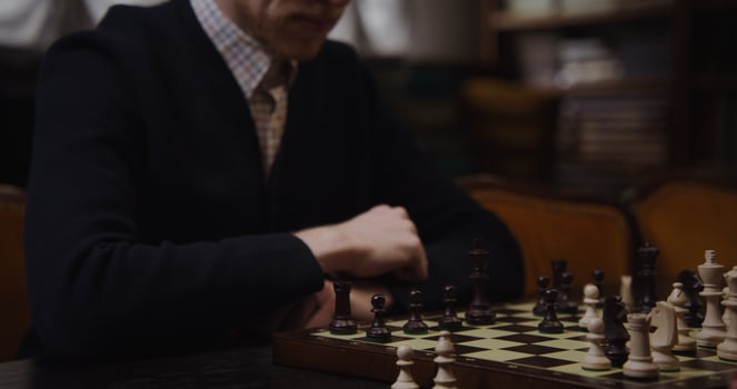 A man in a sweater sitting at a table with a chess board photo