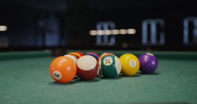 White billiard ball breaks a triangle of colored balls that fly to the sides, one ball flies into the hole, close-up, no people in the - colored photo