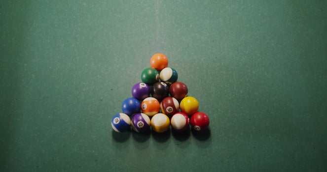 White billiard ball breaks a triangle of colored balls that fly to the sides, one ball flies into the hole, close-up, no people in the photo