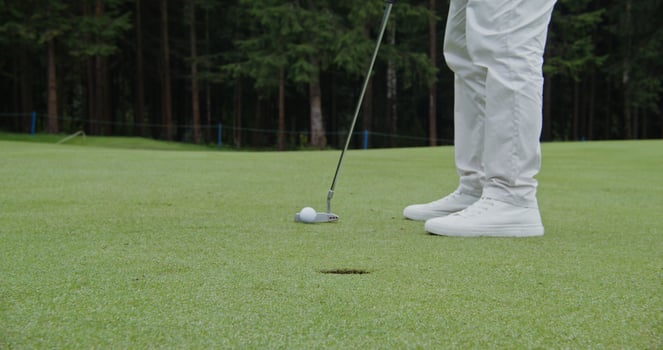 An unidentified man hammers a golf ball into a hole with a golf club, close-up photo