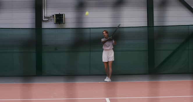 Young woman tennis player, dressed in a white sports uniform, plays tennis, hitting the ball over and over again, actively moving. Filming through a tennis net, the mesh pattern is visible photo
