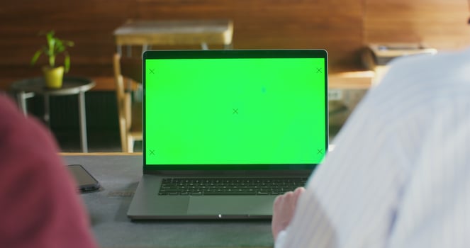 Two people sit at table in a cafe in front of an open laptop with a green screen. Filming from the back. Chroma key, copy space photo