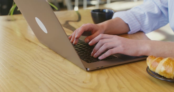 Hands of a fair-skinned woman typing on a laptop sitting at a table in a cafe photo