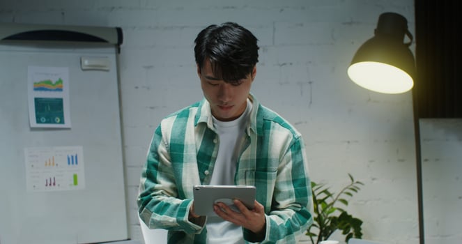 A young man of Asian appearance uses digital tablet, while working in a stylish office and looking up from the screen looking straight into the camera with a smile photo