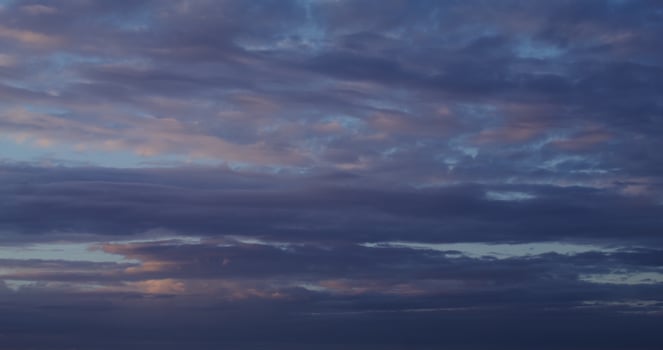 Cloudy sky at sunset. Pink reflections on the clouds slowly floating across the sky over the sea. in 4k, red komodo photo